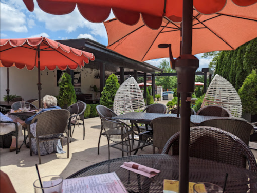 Outdoor dining area with red umbrellas, wicker chairs, and decorative plants, featuring a relaxed atmosphere.